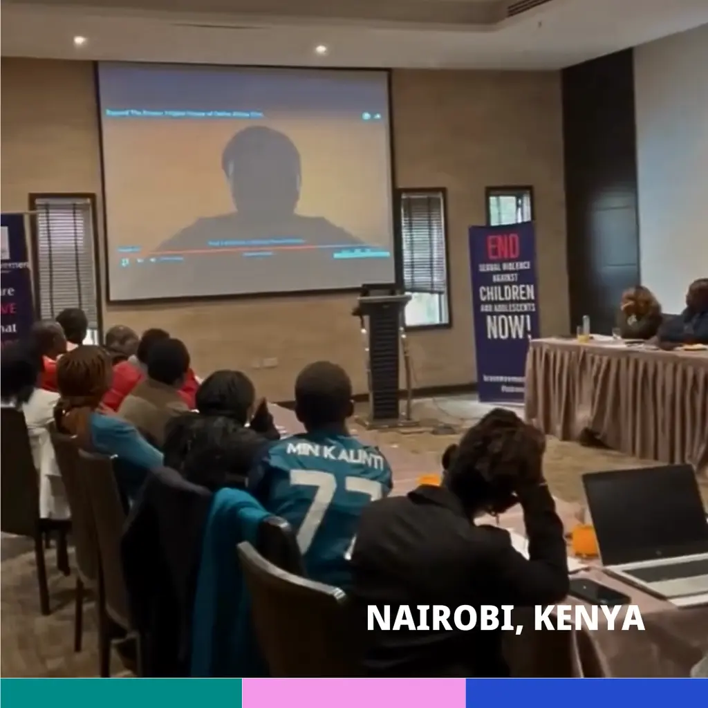 Large projector screen showing a silhouetted figure, audience seated in chairs, banner on table reading "END Childhood Trauma Now!"