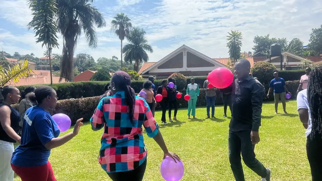 People gathered on a grassy field, holding colourful balloons and umbrellas.