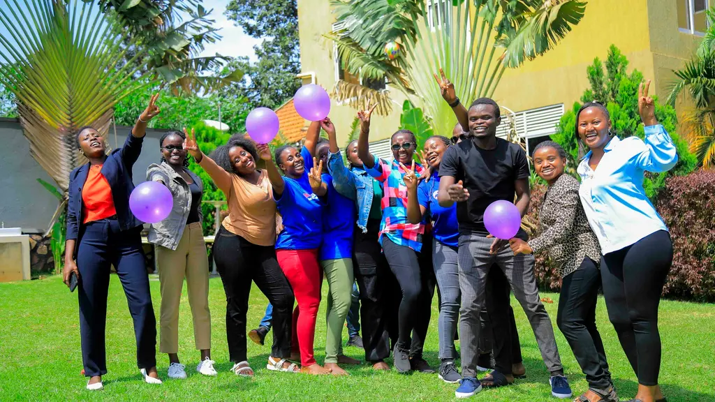 A group of diverse people, dressed in vibrant colours, posing together and holding colourful balloons in an outdoor setting with lush greenery.