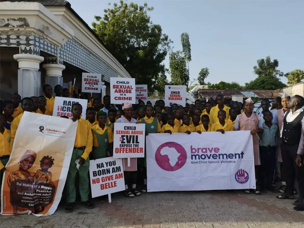 Large group of people in yellow shirts holding signs protesting child sexual abuse and a banner for the "Brave Movement" organization.