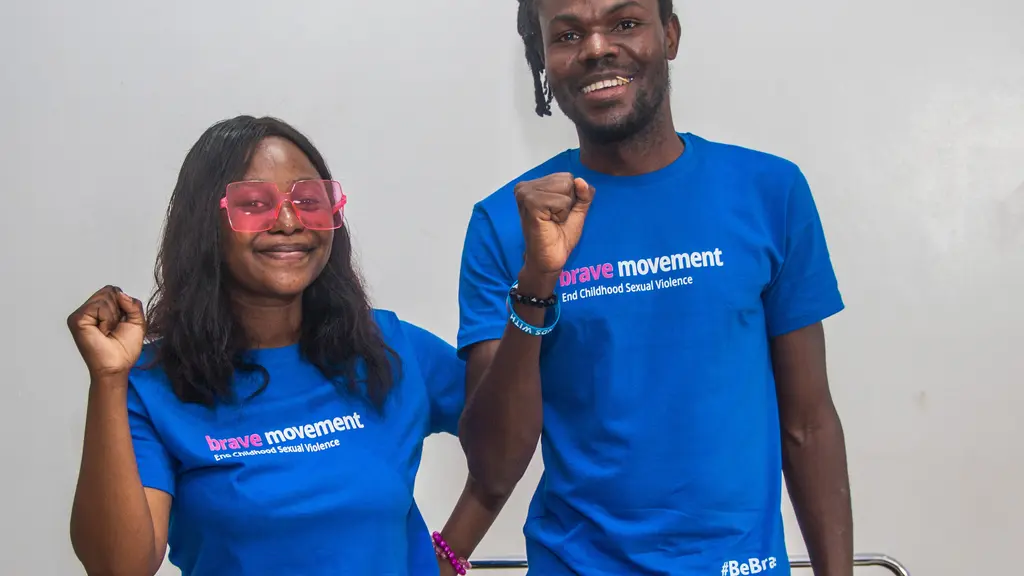 Two people wearing blue "brave movement" t-shirts, smiling and raising their fists.
