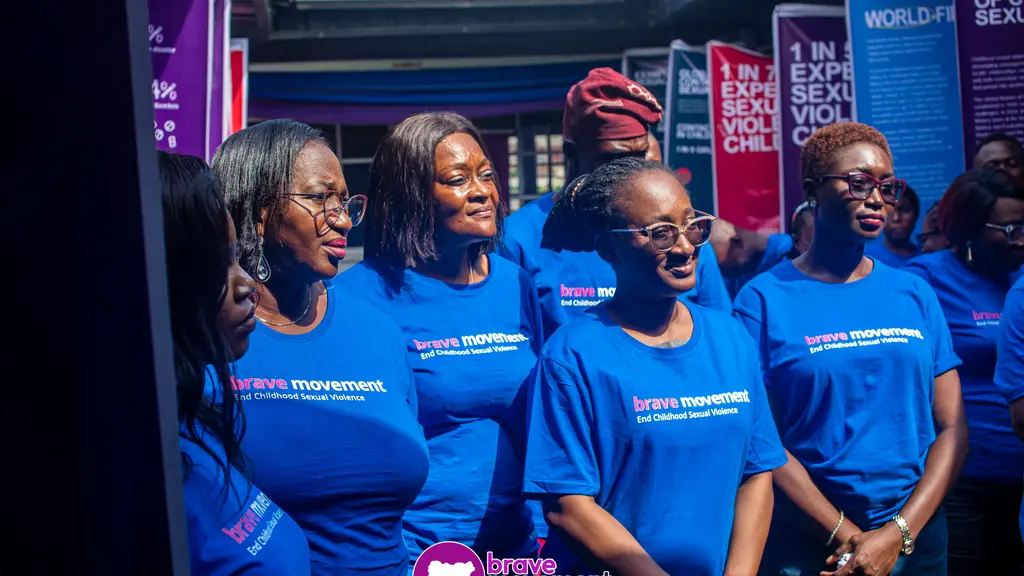A group of 4 women wearing blue t-shirts with the text "Women's Movement" on them, standing in front of colorful posters.