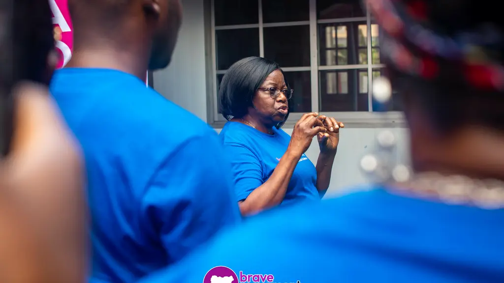 A person in a bright blue shirt speaking into a microphone at what appears to be a rally or event.