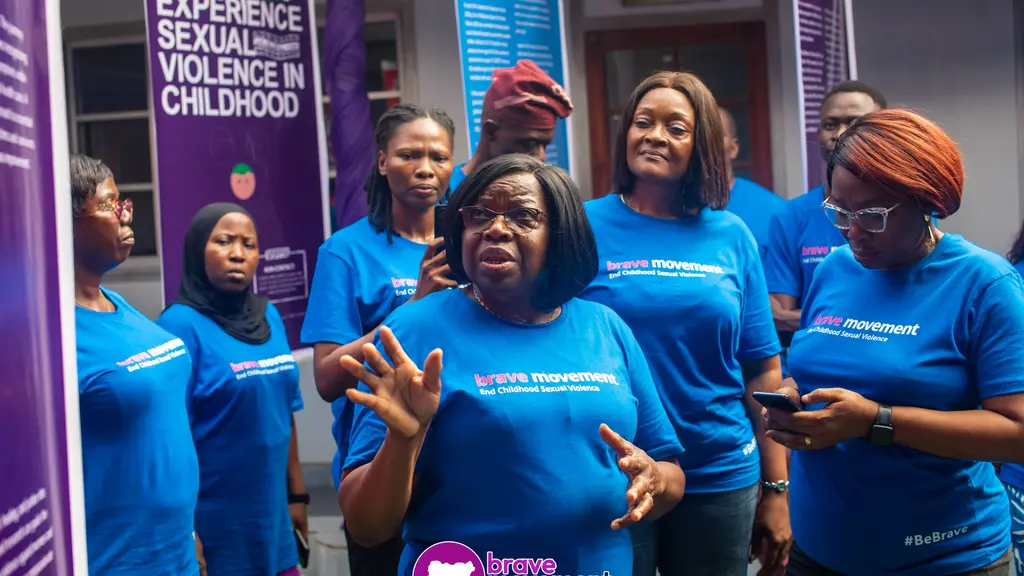 Group of women wearing blue t-shirts with text, standing in front of informational sign about sexual violence against girls.