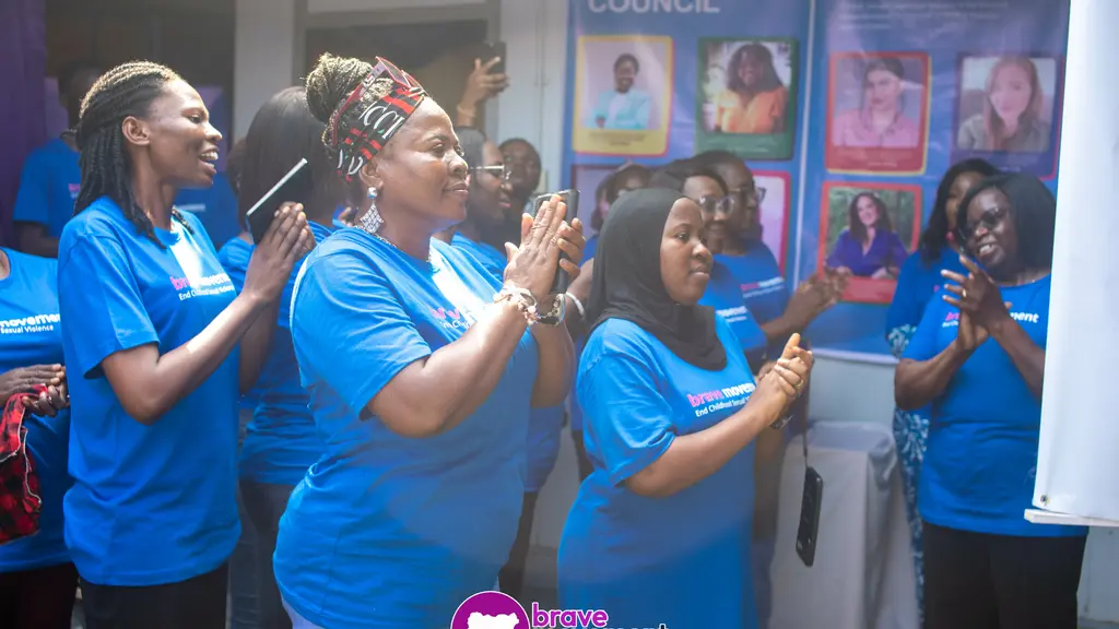 Group of people in blue shirts applauding, standing in front of banners and displays.