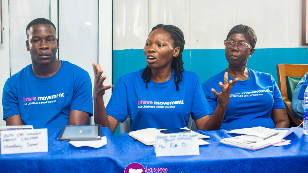 Three people in blue shirts with "Jaye movement" logo, sitting at a table with documents.