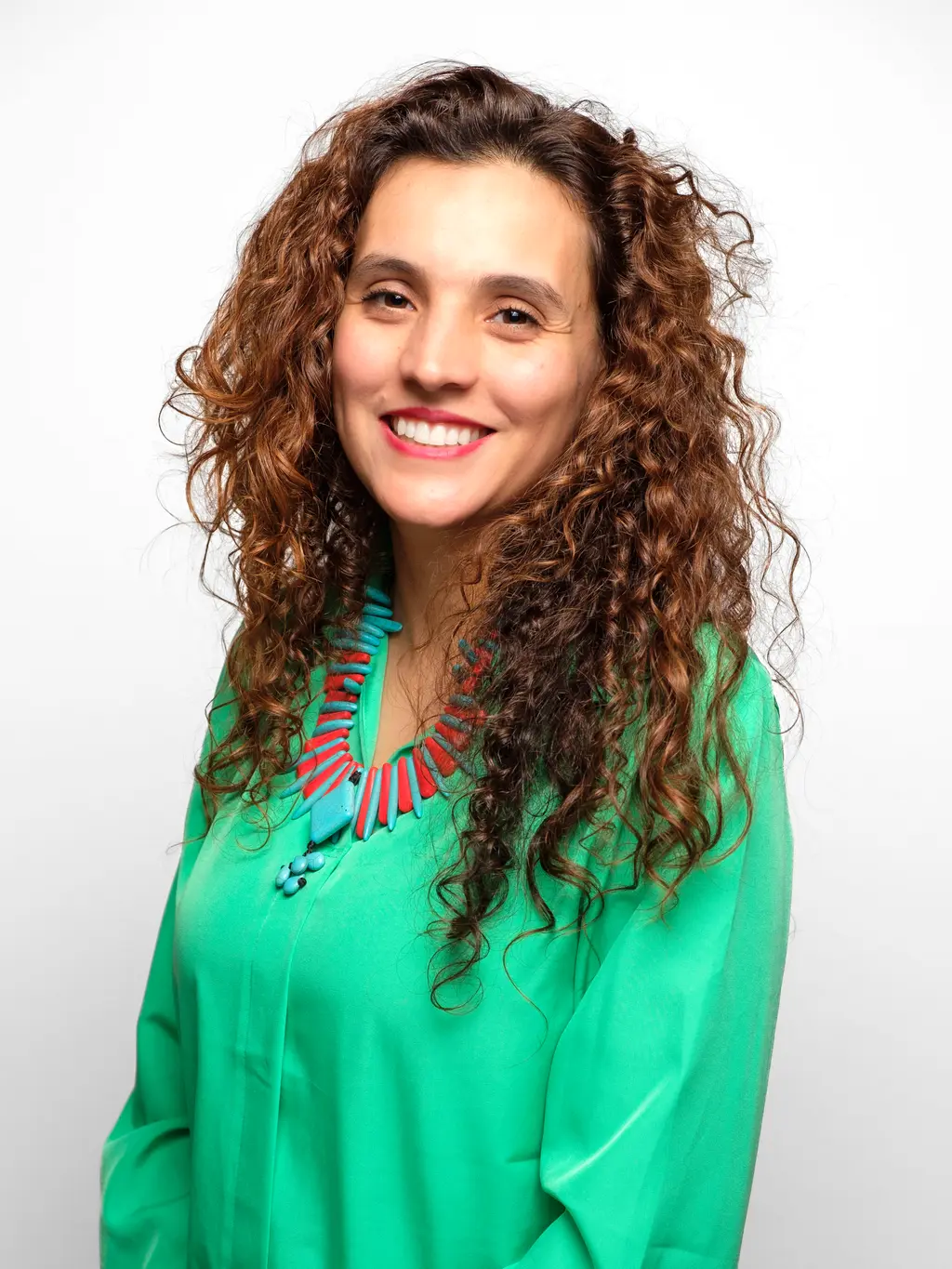 A smiling person with long, curly brown hair wearing a bright green top.