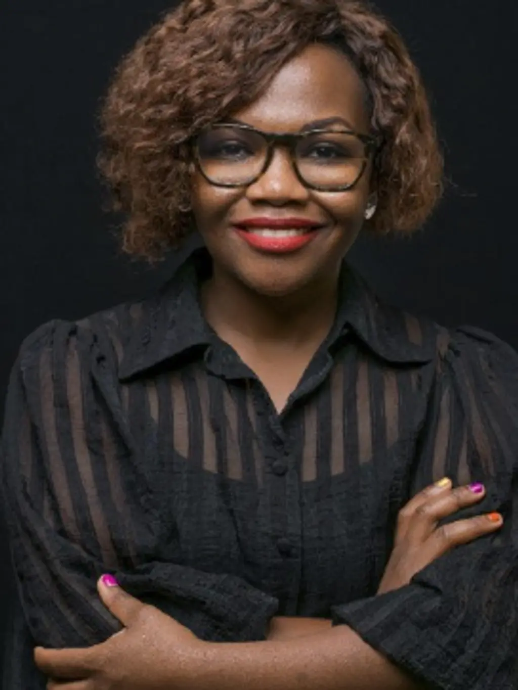 Woman with curly brown hair wearing black-framed glasses and a black shirt, smiling at the camera.