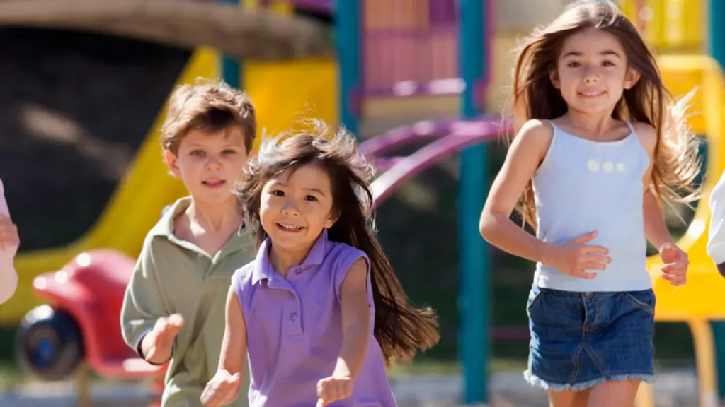 遊び場で走っている4人の子供たち。年齢、性別、人種が異なる。Tシャツやショートパンツを着ており、楽しそうに遊んでいる。背景には遊具や色とりどりの建物が見える。