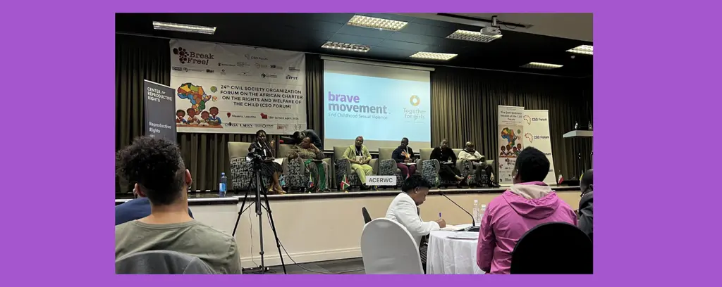 A stage with speakers at a conference, with audience members seated in front of the stage.