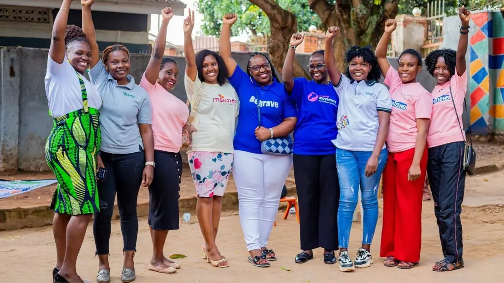 Group of diverse people, dressed casually, standing together with arms raised in celebration, surrounded by a colourful outdoor setting.