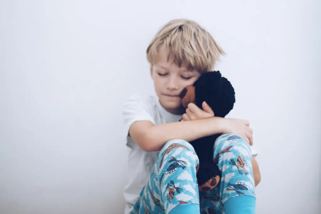 Young child cuddling plush toy, wearing blue patterned pajamas.