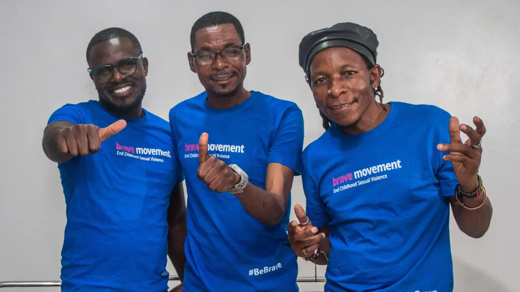 Three people wearing blue t-shirts with "Brave movement" logo, smiling and making hand gestures.