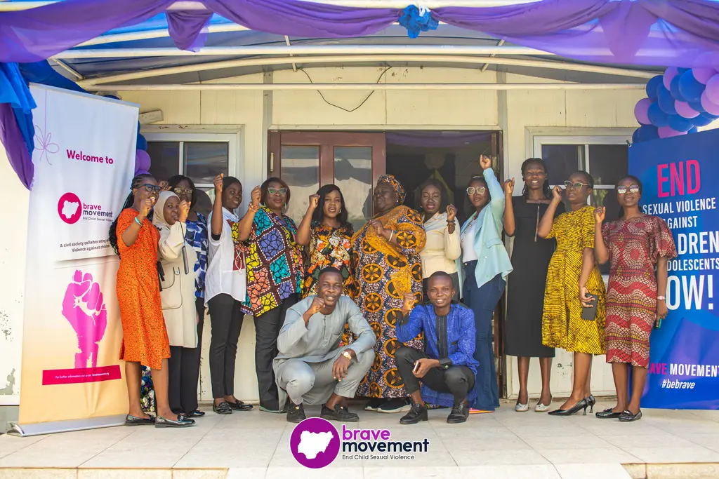 Diverse group of people standing outside a building, with colorful decorations and banners visible.