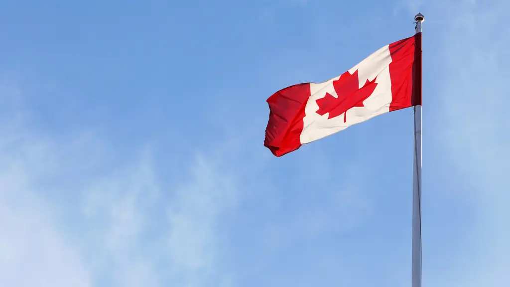 カナダの国旗が青い空に翻っています。赤と白の色が鮮やかで、中央の赤いメープルの葉が特徴的です。旗は風になびき、静かに揺れています。