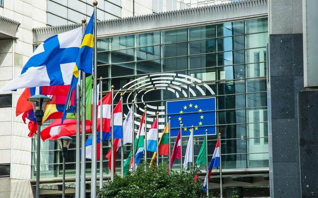 国旗と欧州連合の旗が掲げられているガラスの建物の外観。国旗の色合いは青、赤、白の3色で構成されている。EU旗の星の形も特徴的だ。