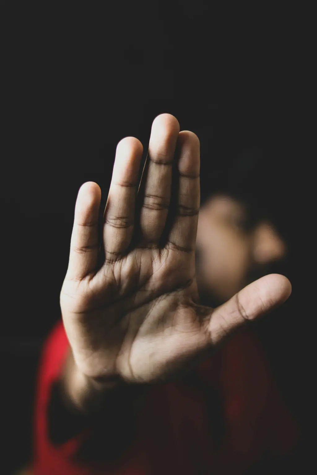 Close-up of hand gesturing 'Stop' against dark background.