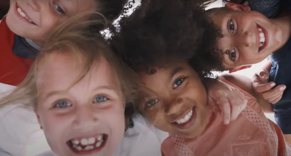 Smiling faces of 3 young girls with different skin tones and hair textures, looking directly at the camera.