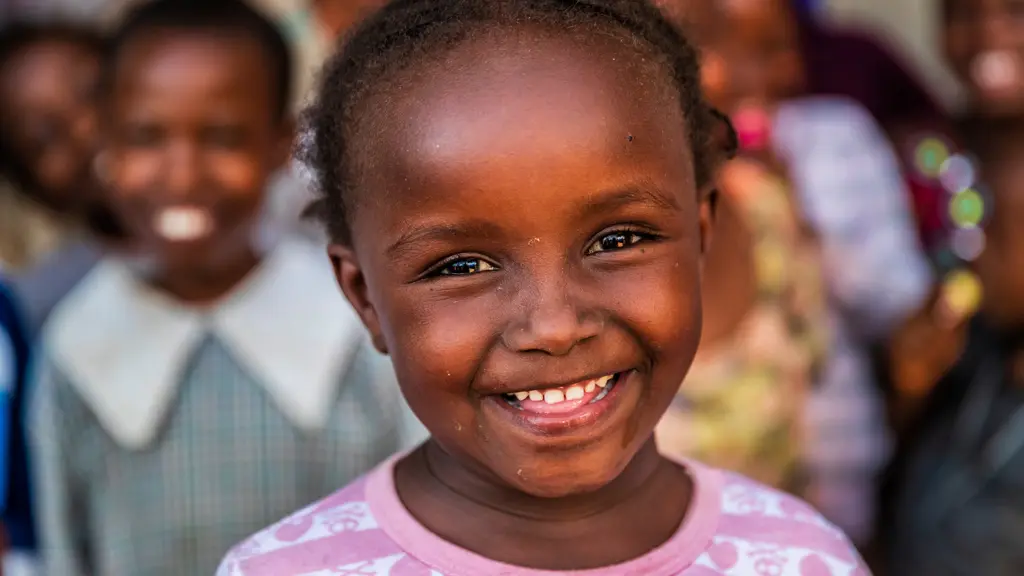A smiling young girl with short dark hair and bright, joyful eyes wearing a pink patterned shirt.